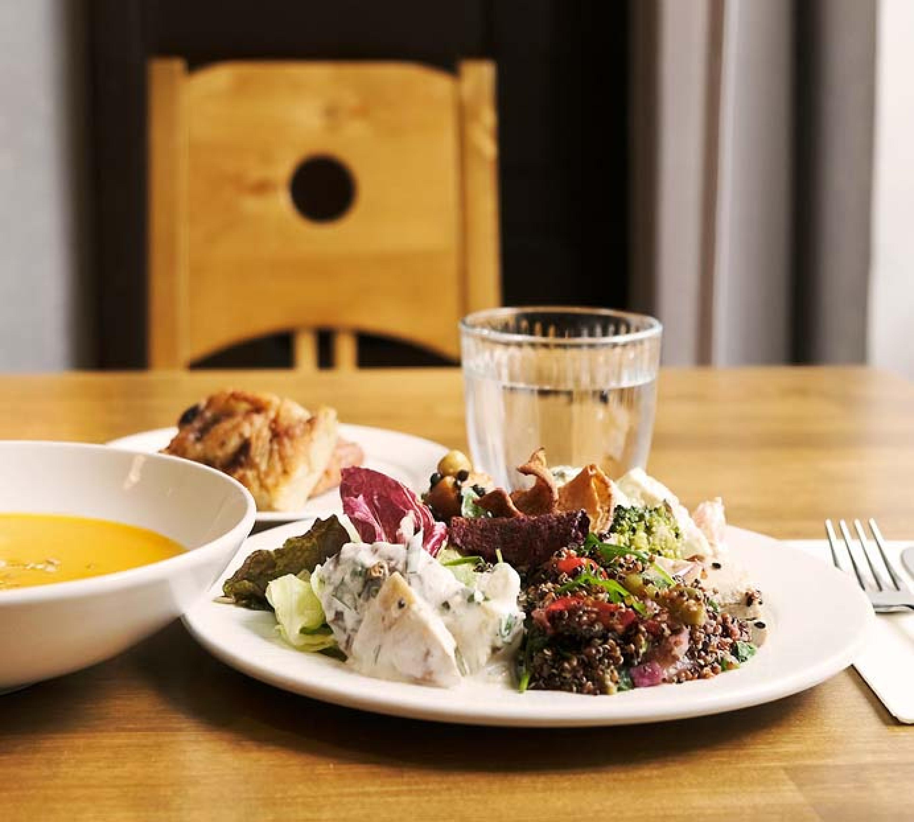 Lautasellinen ruokaa, keittoa ja juomalasi pöydällä.