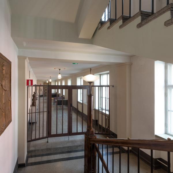 Trappa varifrån en halliknande korridor öppnas i vars främre del stängda portdörrar.