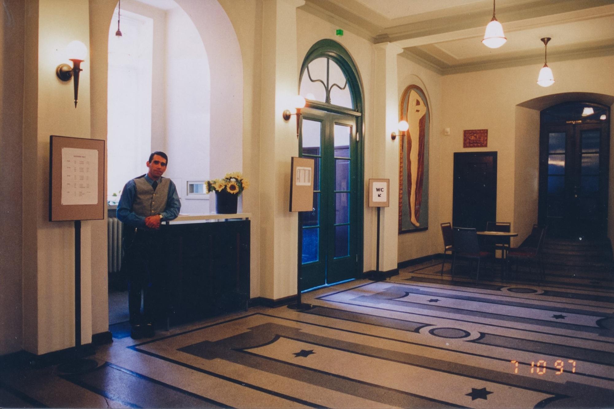 Miesoletettu henkilö nojaa tiskiin suuressa aulassa.