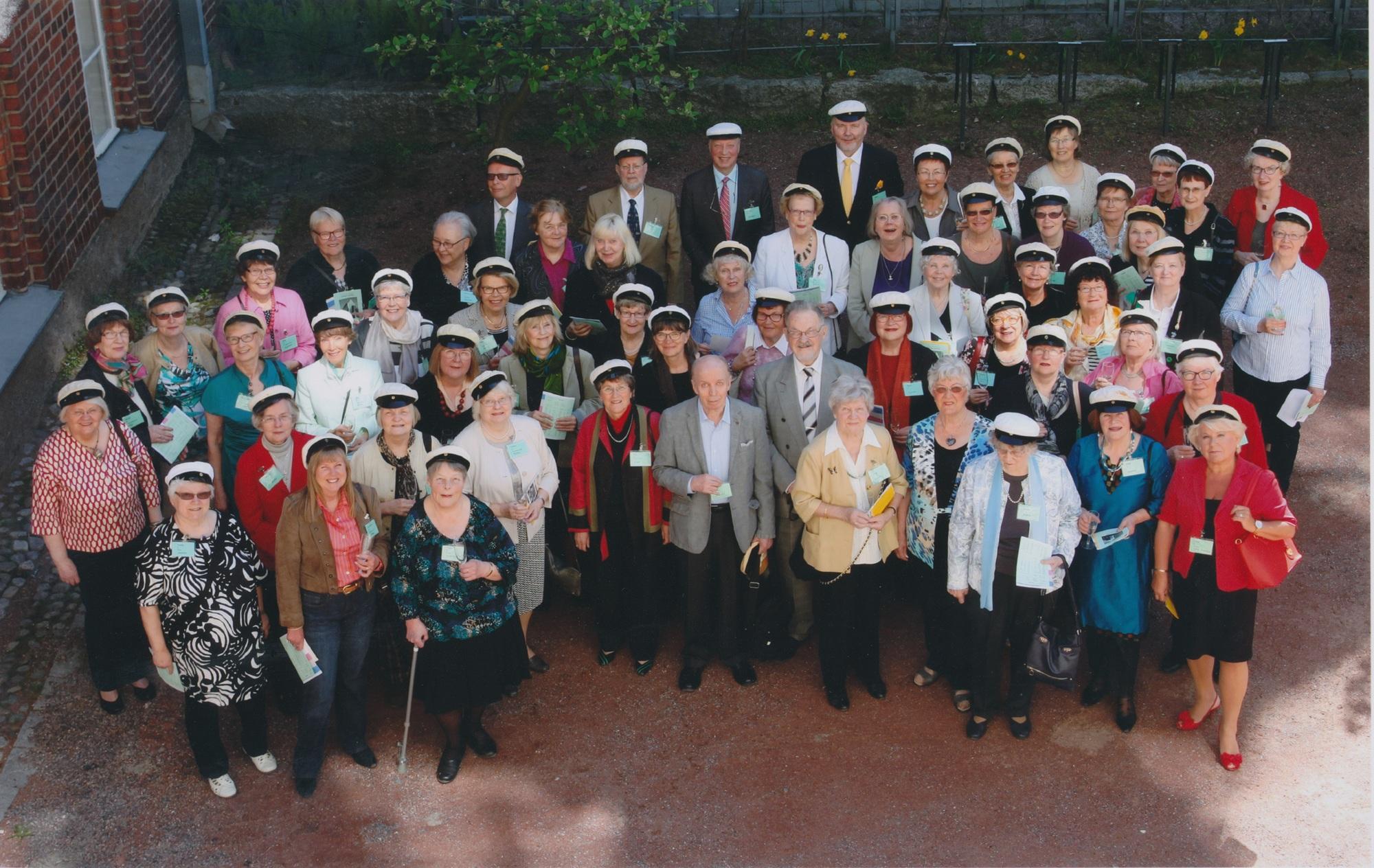 Ihmisiä seisoo pihalla valkolakit päässään.