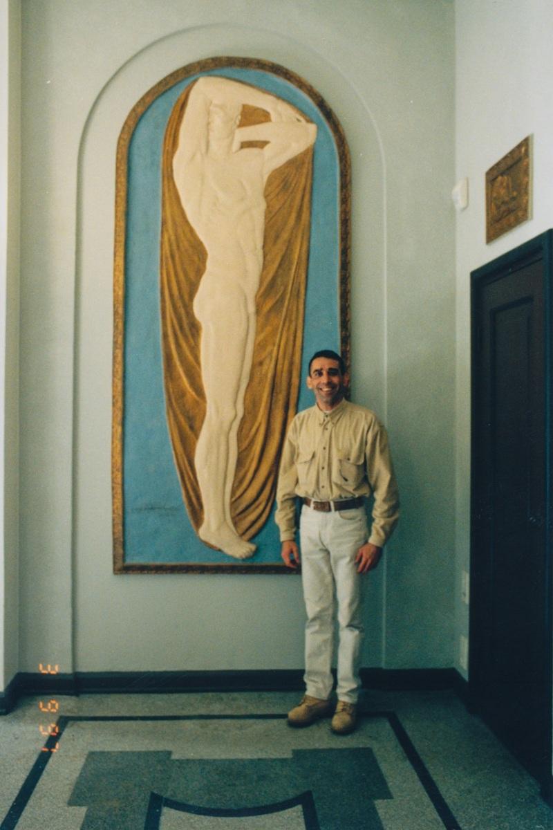 Miesoletettu henkilö poseeraa ison reliefin vieressä.