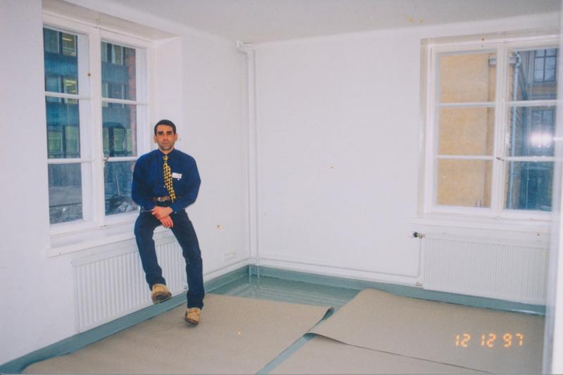 Miesoletettu henkilö istuu ikkunalaudalla, lattialla suojapapereita.