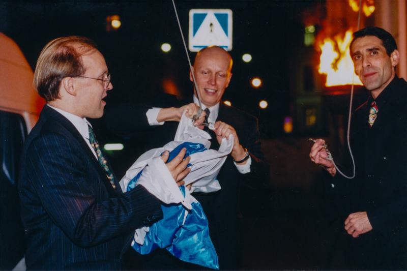 Kolme miesoletettua henkilöä kiinnittämässä Suomen lippua.