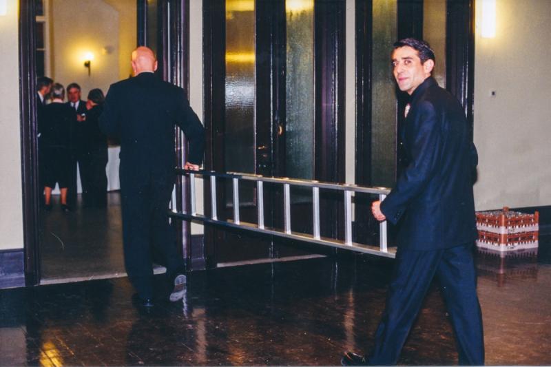 Kaksi miesoletettua henkilöä kantaa siistit vaatteet päällään tikapuita.