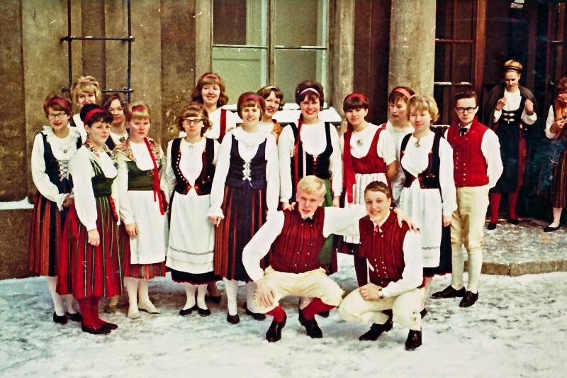 Kansallispukuisia nuoria rakennuksen edustalla, lunta maassa.