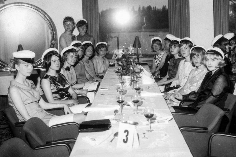 Ylioppilaita hienosti pukeutuneena pitkän pöydän äärellä.